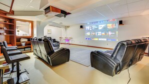 A modern room with leather reclining chairs, a large screen displaying a movie, and a wooden bookshelf. - Sauna, Pickleball Court & Game Room: Sultan Villa! (Sultan)