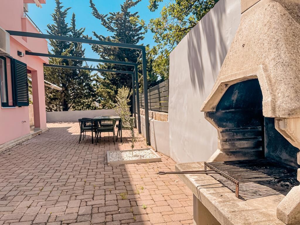 A patio area with a stone oven, outdoor seating, and a pink building in the background.
