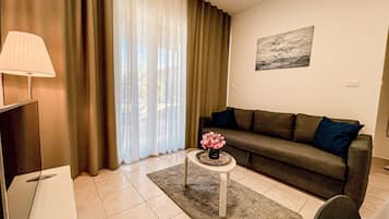 A living room with a sofa, a coffee table with a vase of flowers, a lamp, and a painting on the wall.