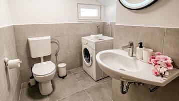 A modern bathroom with a toilet, washing machine, sink, and a mirror with a light.