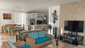 Una sala moderna con muebles de mimbre, un televisor de pantalla plana y una cocina al fondo.