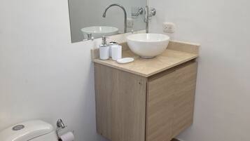 Een badkamer met een wit toilet, een wastafel met een grote spiegel erboven en een houten kastje eronder.
