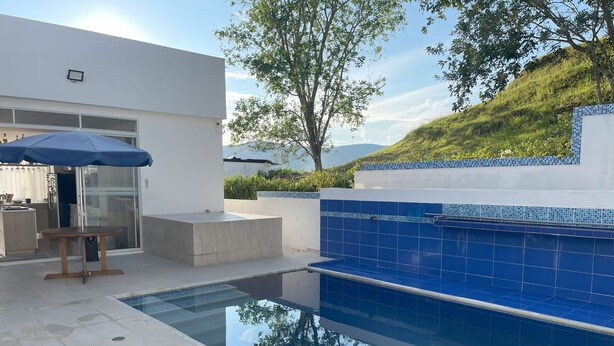 Un área de piscina moderna al aire libre, con vista despejada a la piscina, una mesa de madera y un muro de azulejos azules.