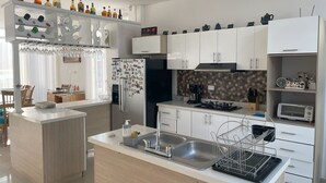 Una cocina moderna con una isla central, muebles blancos, horno integrado y una cafetera.