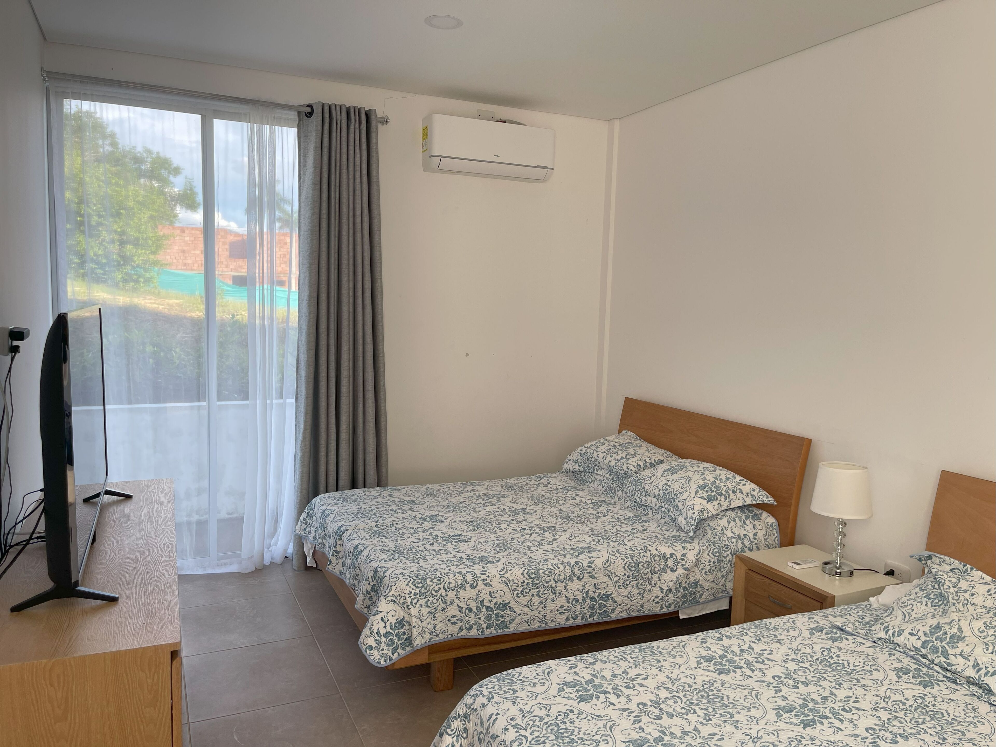 Habitación de hotel con dos camas, televisión, escritorio y aire acondicionado.