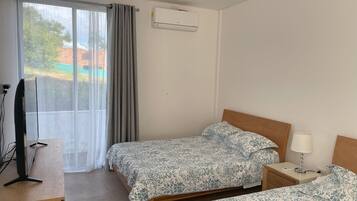 Habitación de hotel con dos camas, televisión, escritorio y aire acondicionado.