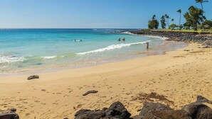 A sandy beach with clear blue water, a few people, and palm trees. - Newly Renovated, Ocean Views, Minutes to Beach (Koloa)