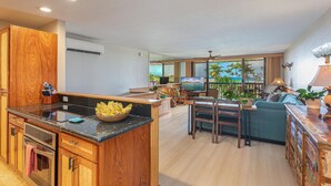 A modern kitchen with wooden cabinets, a central island, and a dining area with a view of the ocean. - Newly Renovated, Ocean Views, Minutes to Beach (Koloa)
