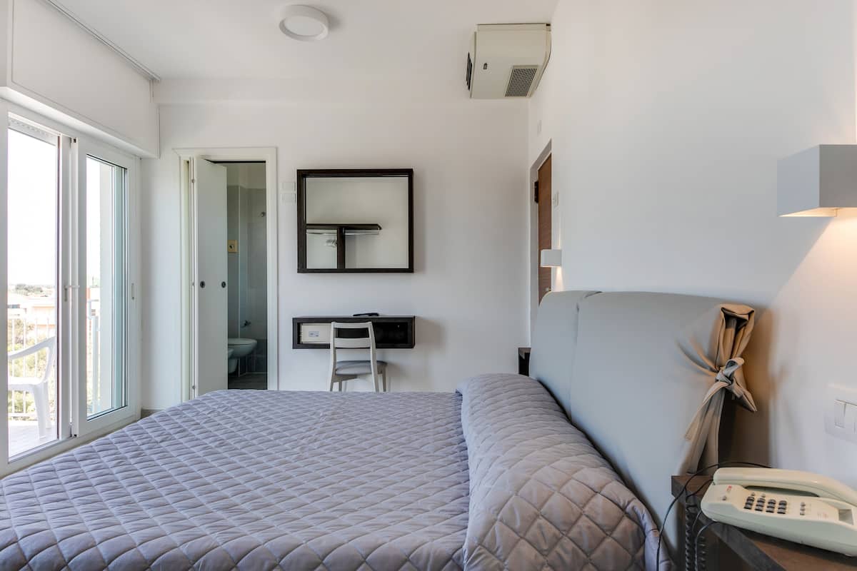 A hotel room with a large bed, a desk with a chair, a telephone, and a view of the outdoors.