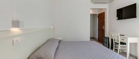 Un dormitorio con cama, escritorio, silla, televisión y una puerta que da a otra habitación.