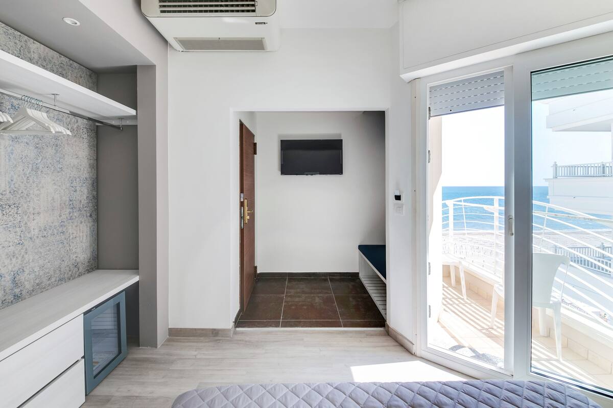 A modern hotel room with a balcony, a TV mounted on the wall, and a wooden door leading to the balcony.