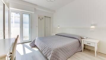 Quarto com cama, mesa de cabeceira, cadeira e porta de vidro deslizante para uma varanda.
