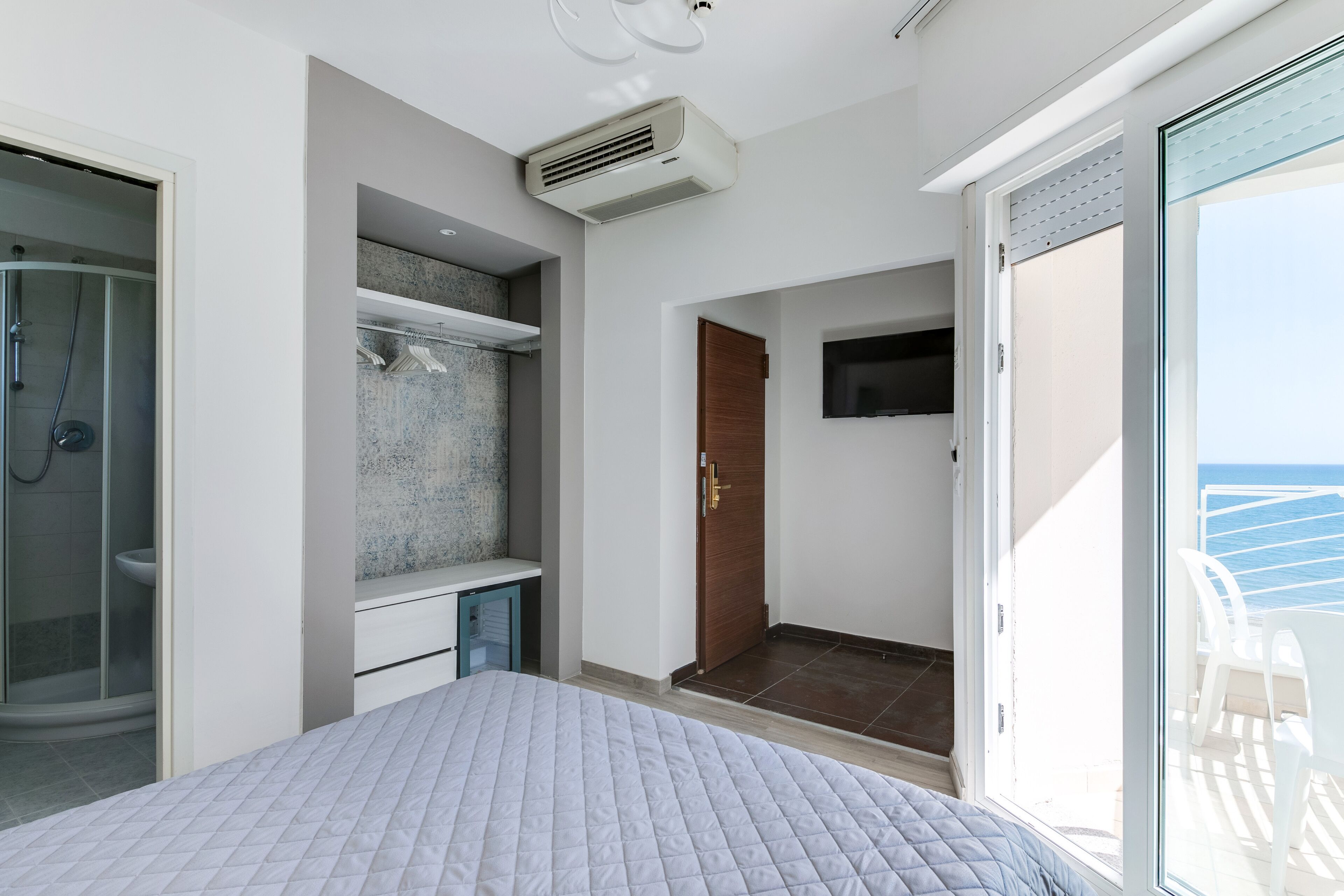 A bedroom with a bed, a shower, a TV, and a balcony with a view of the sea.