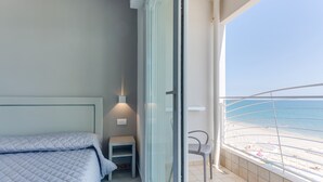 A bedroom with a bed, a nightstand, and a chair by a balcony with a view of the beach. - Marittimo Riccione (Riccione)