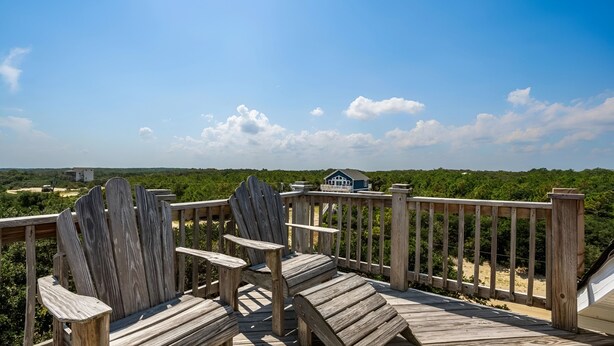 A wooden deck with two Adirondack chairs, overlooking a beach and a house in the distance. - Skyview by the Sea (Corolla)