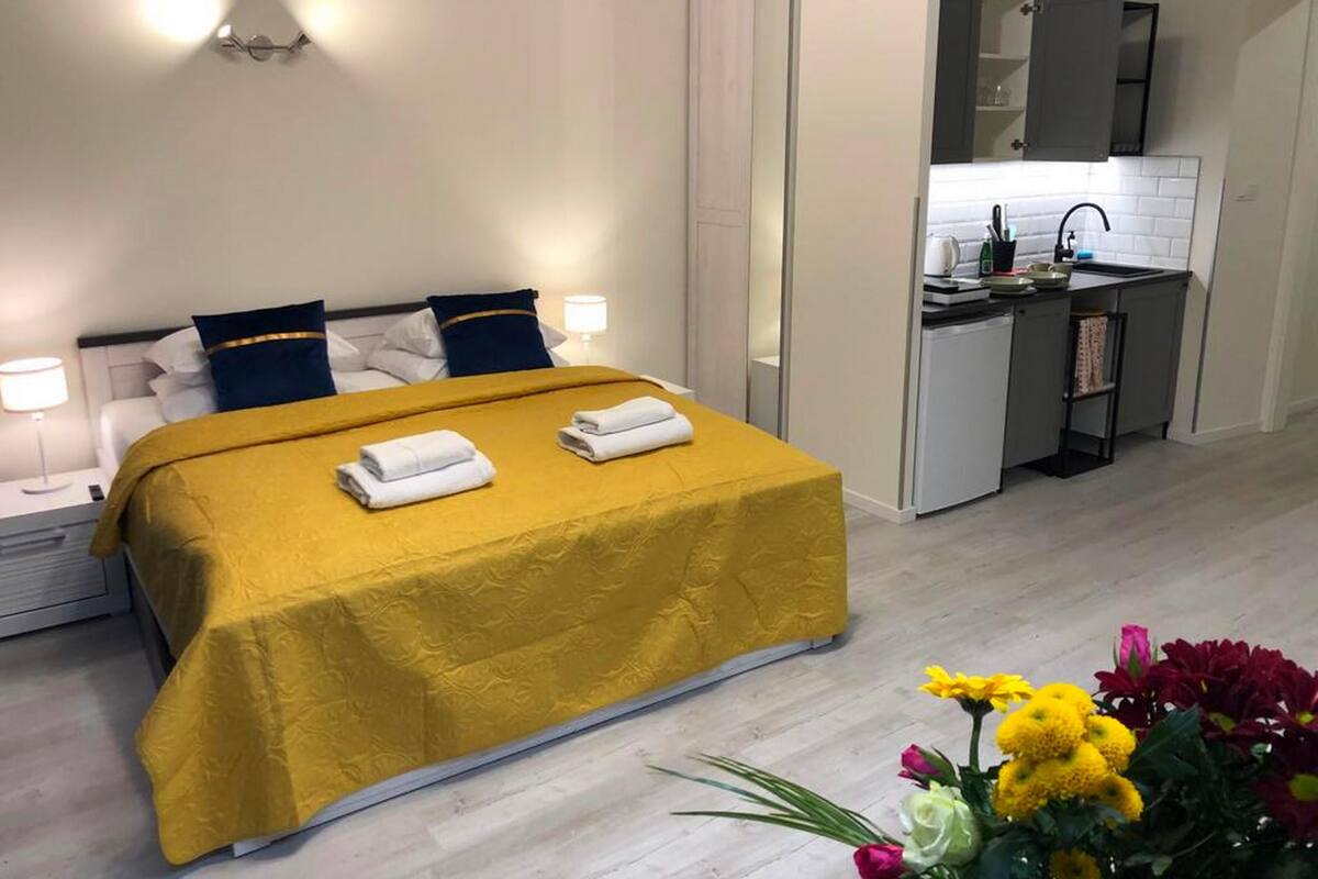Una habitación de hotel con cama, mesitas de noche, una kitchenette pequeña y un baño.