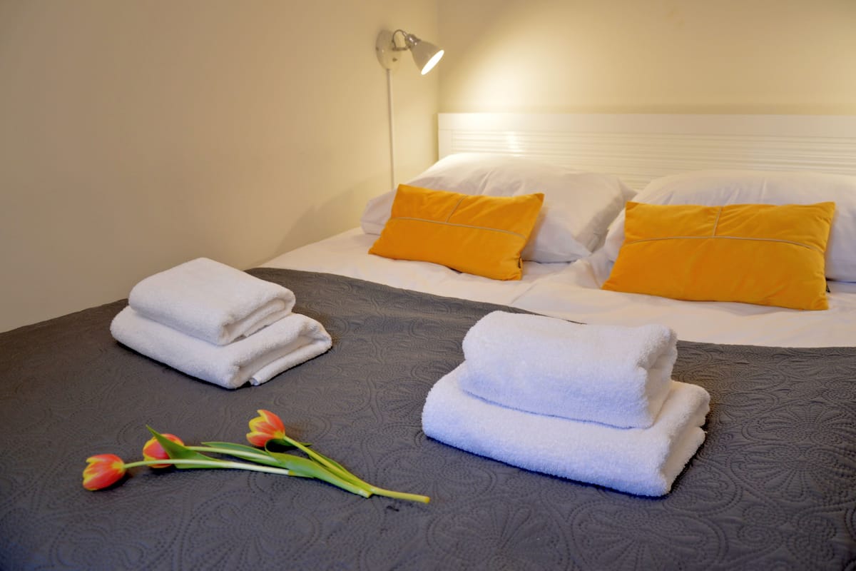 Habitación de hotel con dos camas, cada una con almohadas blancas y amarillas, y toallas dobladas sobre las camas.