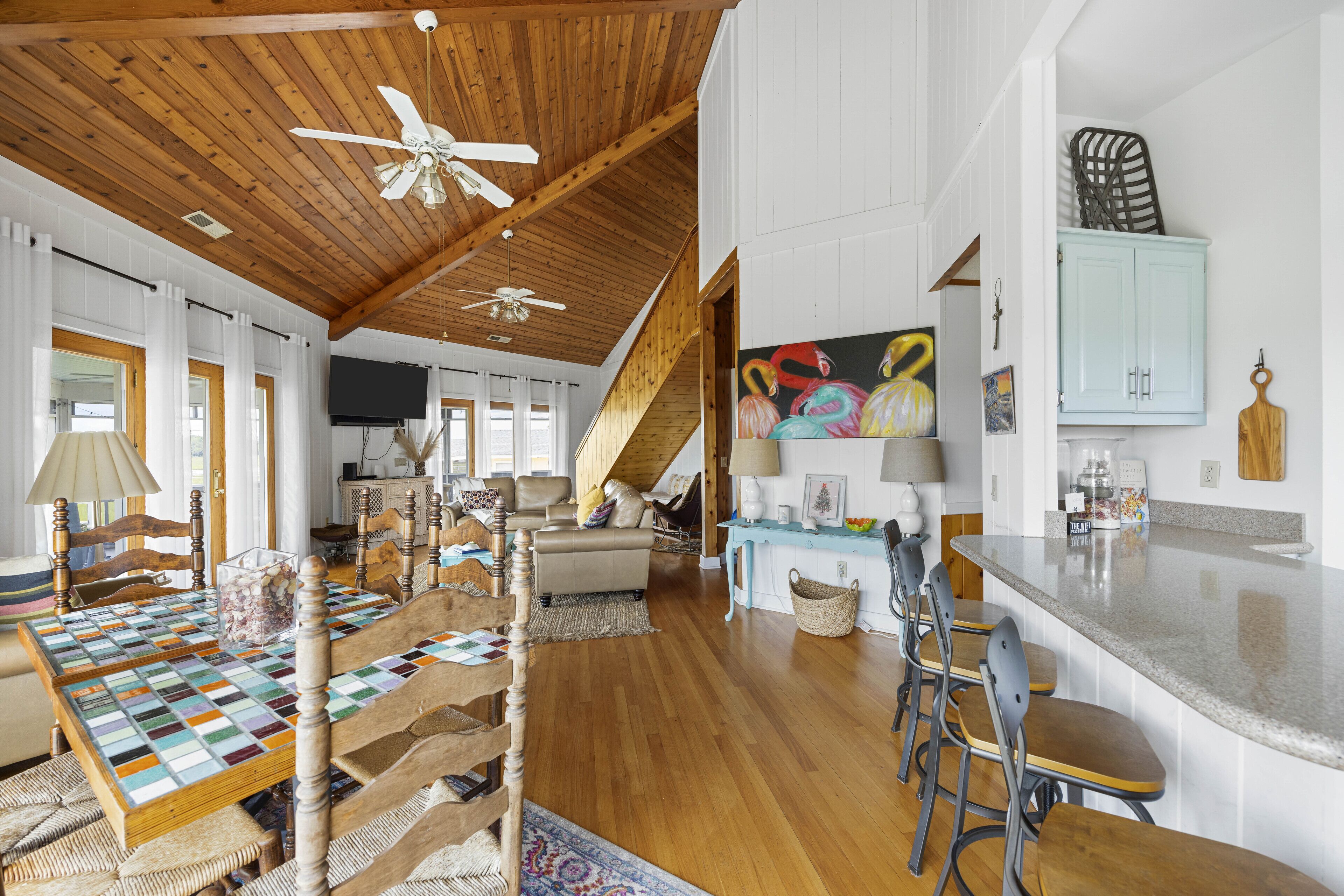 A spacious living area with a wooden ceiling, a dining table with chairs, a sofa, and a television.