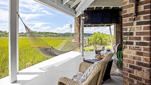 Eine überdachte Terrasse mit einer Hängematte, Korbmöbeln und Blick auf ein grünes Feld.