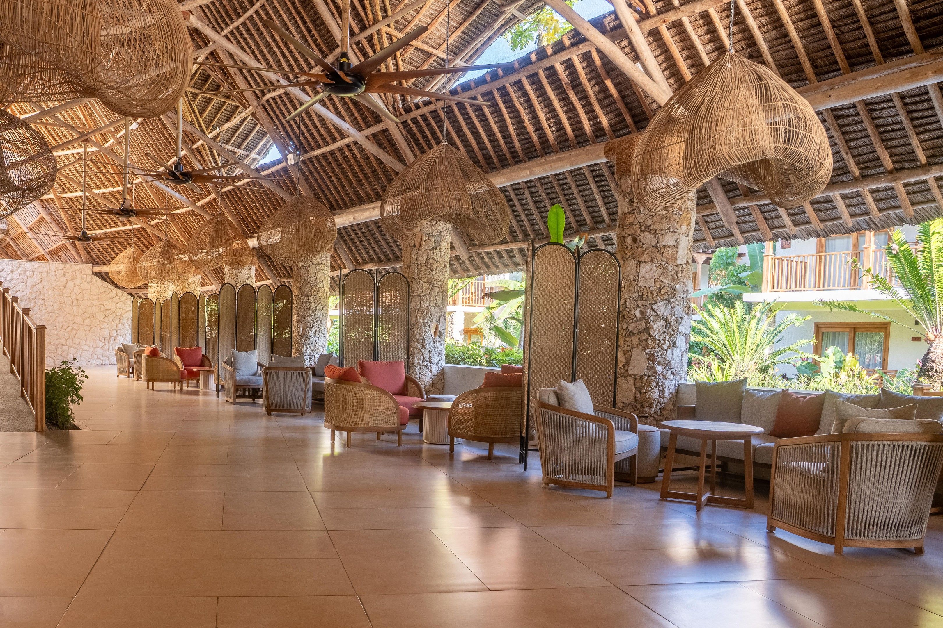 A spacious indoor area with wicker furniture, stone pillars, and a high ceiling with wooden beams.