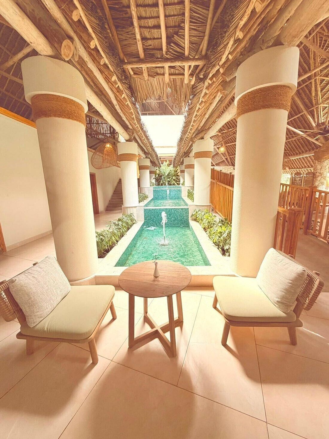 A pool area with two lounge chairs and a table, surrounded by columns and a thatched roof.