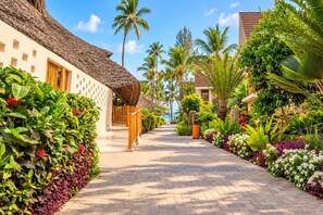 A pathway lined with lush greenery and palm trees, leading to a building with a thatched roof. - JAZ Amaluna - Adults Only 16+ (Uroa)