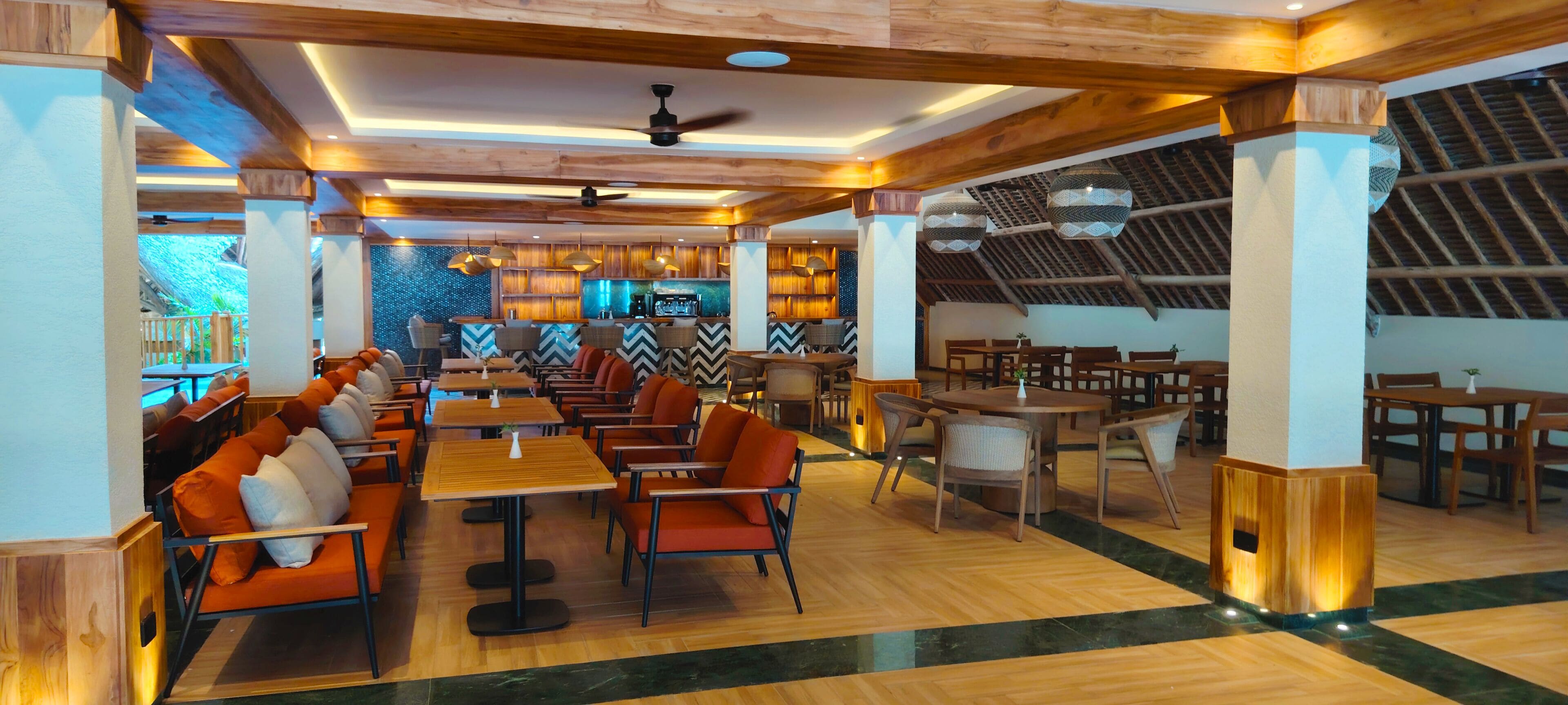 A spacious restaurant with wooden flooring, multiple seating areas, and a bar in the background.