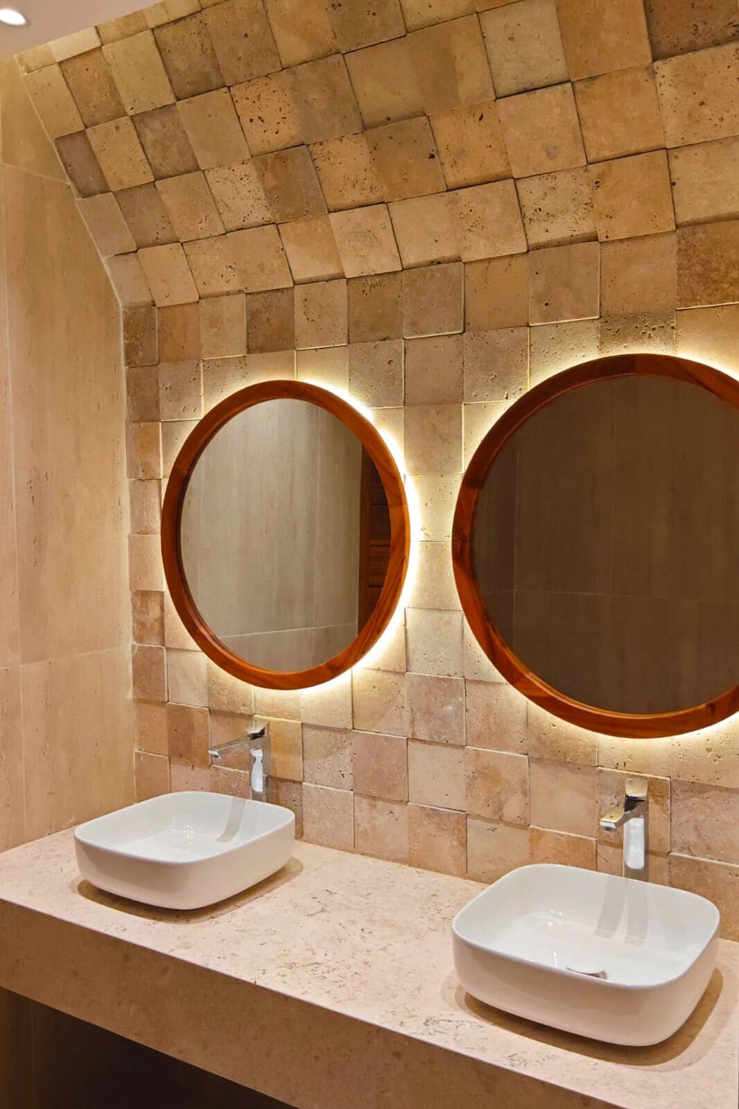 A bathroom with two sinks, a tiled wall, and a wooden-framed mirror.