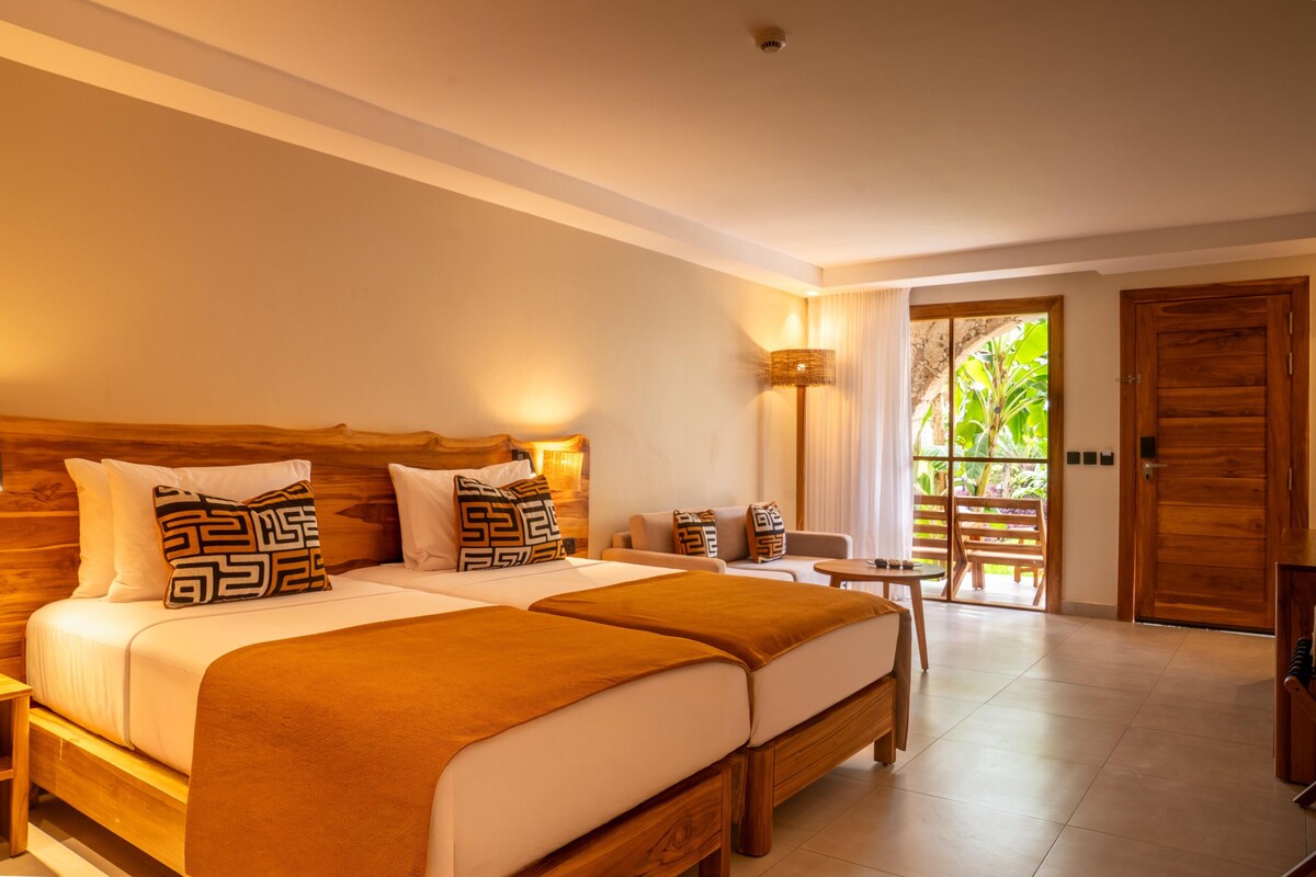 A hotel room with a large bed, a small table, and a view of the outdoors.