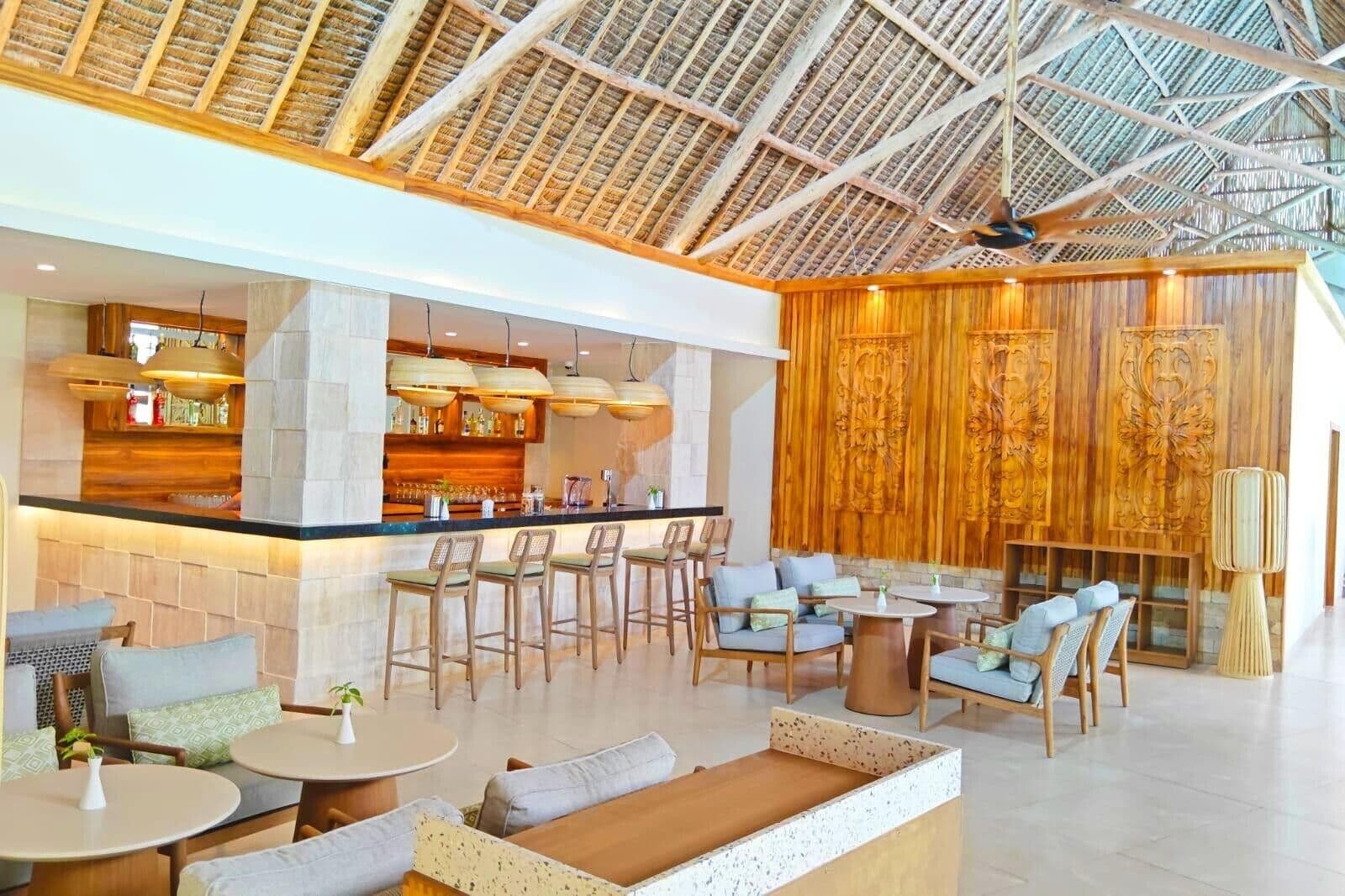 Eine geräumige Lobby mit Barbereich, Sitzgelegenheiten und einer hohen Decke im Design eines Strohdachs.
