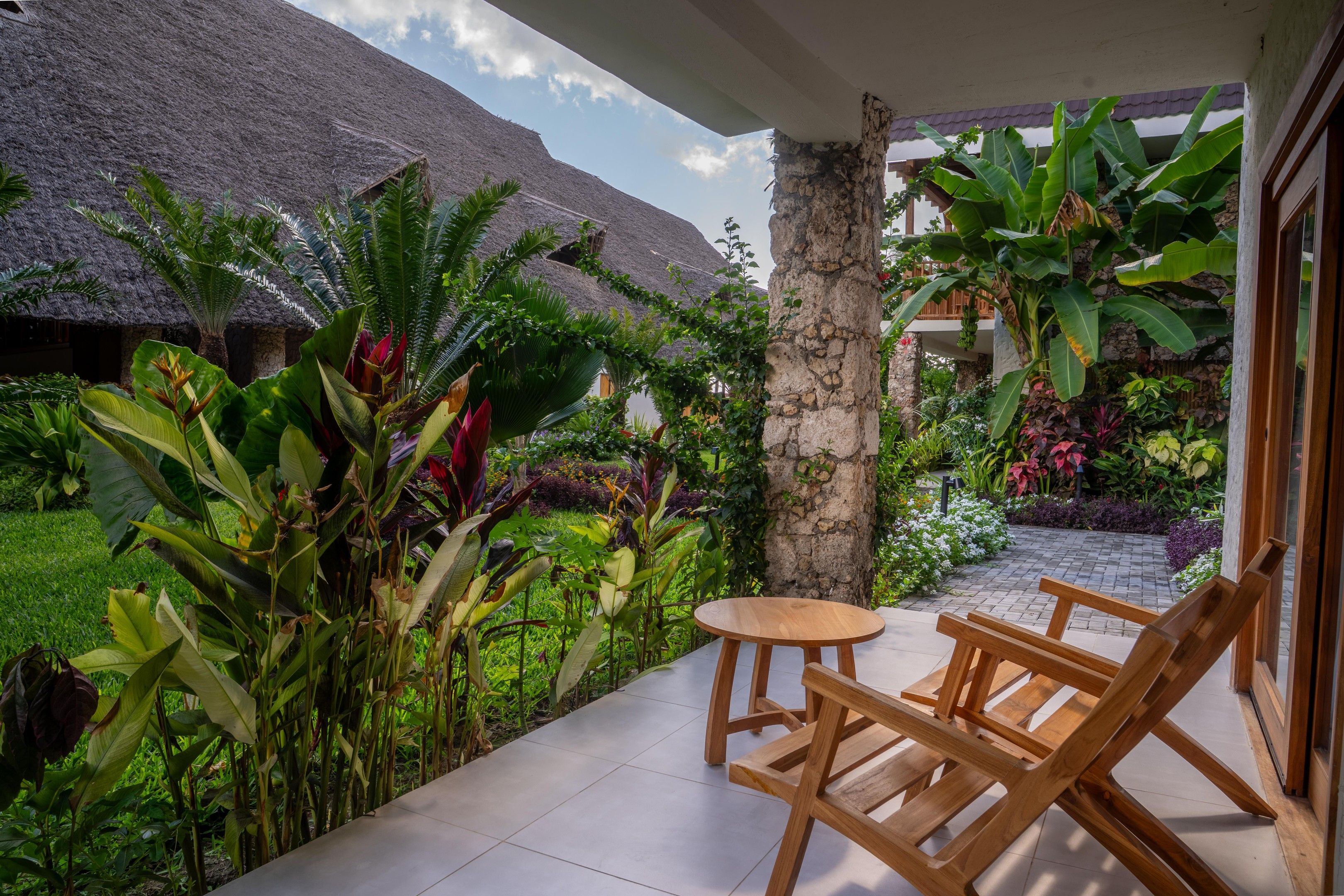 Une terrasse avec une table et des chaises, entourée d’une végétation tropicale luxuriante et d’une structure à toit de chaume.