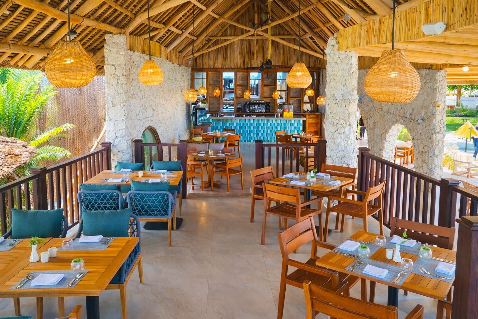 A restaurant with wooden tables and chairs, hanging wicker lamps, and a stone wall.