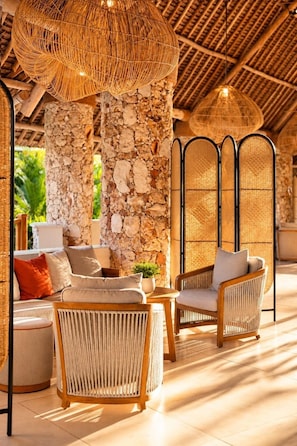 A cozy outdoor seating area with wicker furniture, a stone wall backdrop, and a thatched ceiling. - JAZ Amaluna - Adults Only 16+ (Uroa)