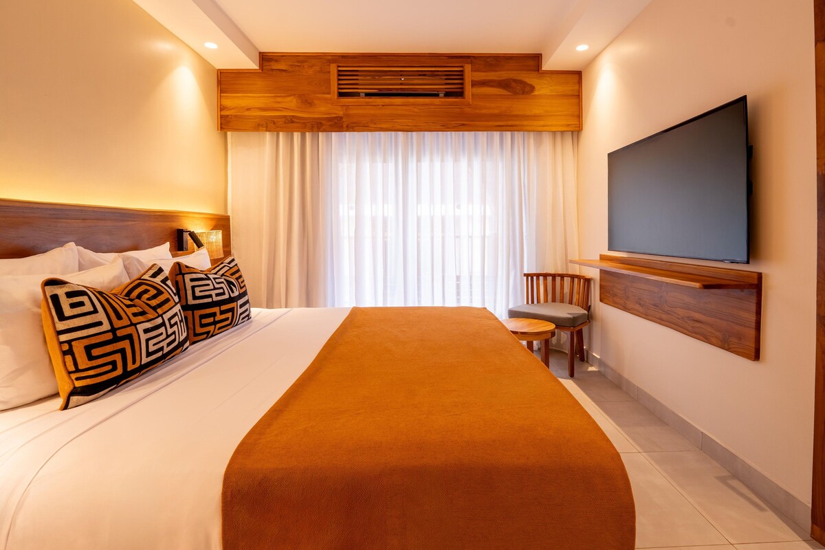 A hotel room with a bed, a TV mounted on the wall, and a chair.