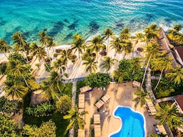Vista aérea de un resort con piscina, palmeras y una playa.