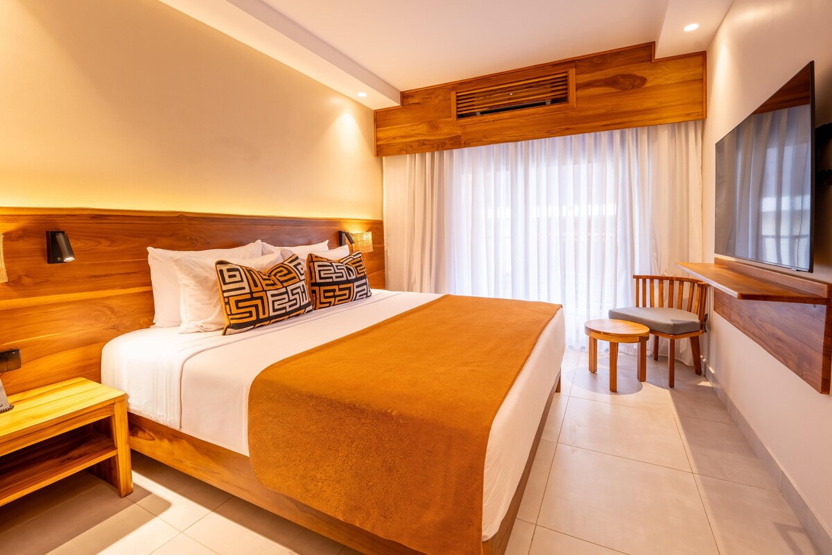 A modern hotel room with a large bed, a TV, a desk, and a chair.
