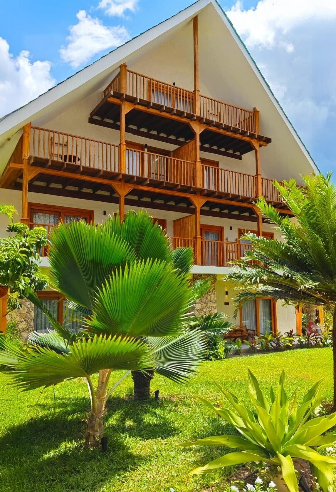 Un immeuble à plusieurs étages doté de balcons en bois et d’un jardin planté de plantes tropicales.