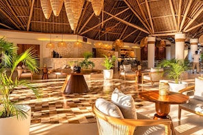 A spacious lobby with a checkered floor, round tables, wicker furniture, and a high ceiling with bamboo beams. - JAZ Amaluna - Adults Only 16+ (Uroa)