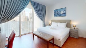 A hotel room with a large bed, a bench, a nightstand, and a view of the city through floor-to-ceiling windows. - La Vie - Spacious One Bedroom (Jumeirah Beach Residence)
