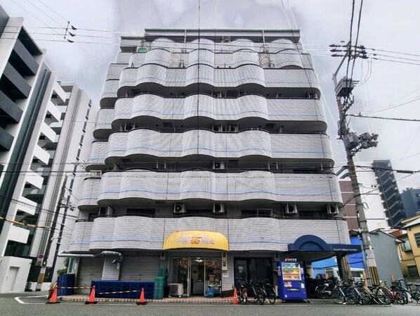 Ein mehrstöckiges Gebäude mit einer markanten, gewölbten Fassade, einem sichtbaren Laden mit Beschilderung und einer Reihe Fahrrädern vor der Tür.