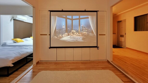 A bedroom with a large window, a bed, and a projection screen displaying a cityscape. - Grand Colbert NANBA 301, 303, 404, 602 (Osaka)