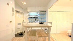 A compact kitchen with white cabinets, a wooden dining table with chairs, and a small countertop with appliances. - Grand Colbert NANBA 301, 303, 404, 602 (Osaka)