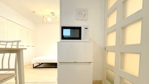 A compact room with a white refrigerator, a microwave, a small table, and a bed. - Grand Colbert NANBA 301, 303, 404, 602 (Osaka)