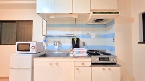 A compact kitchen with white cabinets, a microwave, a small refrigerator, a sink, and a stove. - Grand Colbert NANBA 301, 303, 404, 602 (Osaka)