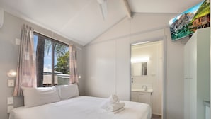 A bedroom with a large bed, a window with curtains, a bathroom with a mirror and sink, and a TV mounted on the wall.