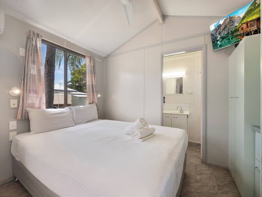 Une chambre avec un grand lit, une fenêtre avec des rideaux, une salle de bain avec un miroir et un lavabo, et un téléviseur fixé au mur.