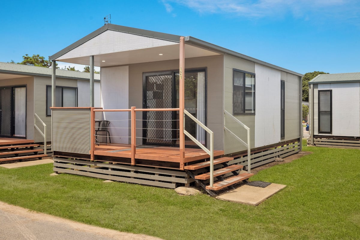 A single-story mobile home with a covered porch, a small deck, and a front door.