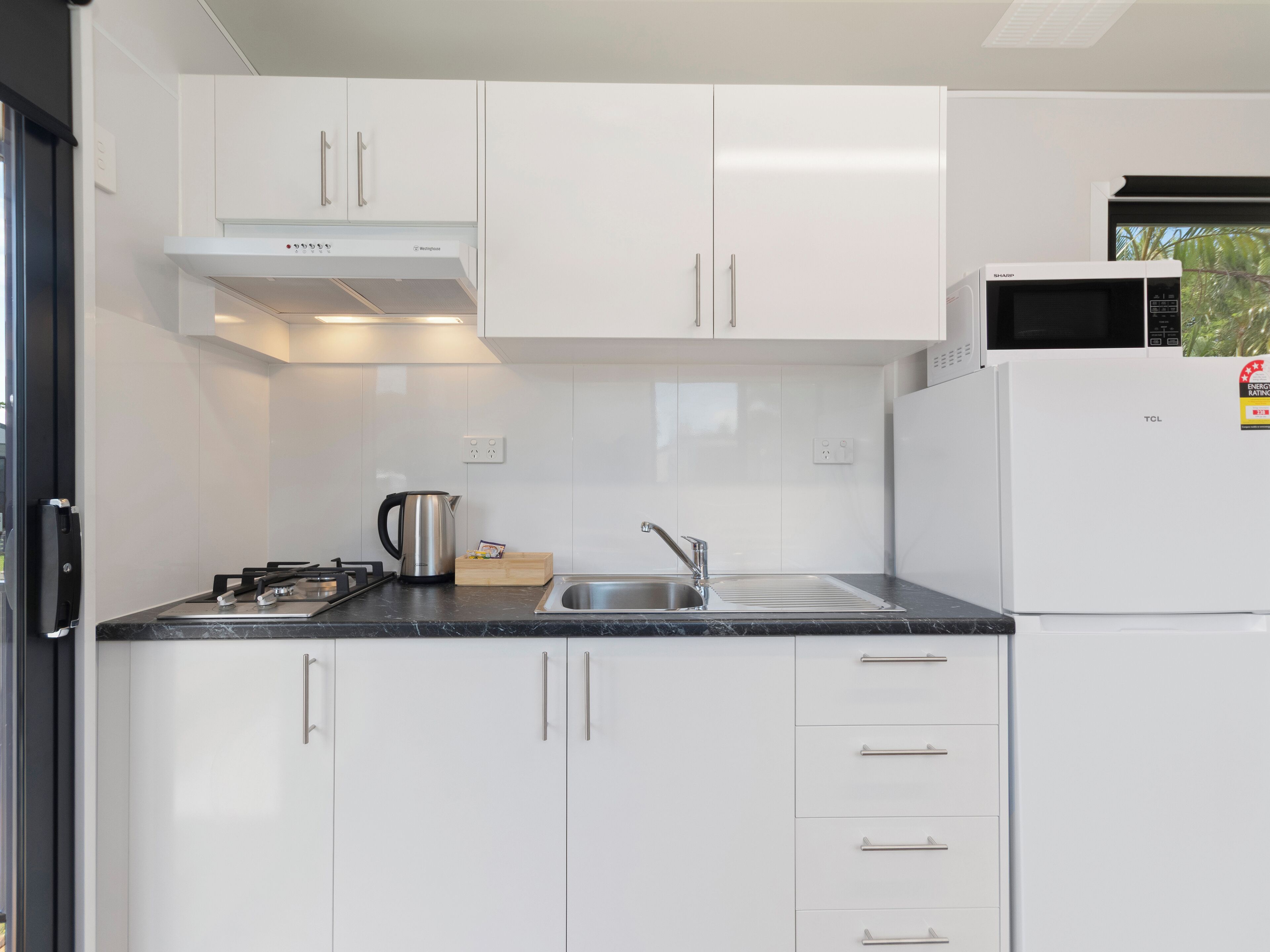 A modern kitchen with white cabinets, a stainless steel sink, a microwave, and a kettle.