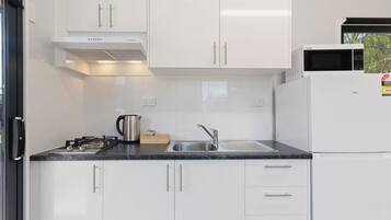 A modern kitchen with white cabinets, a stainless steel sink, a microwave, and a kettle.