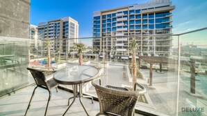 Un balcon agrémenté de fauteuils en osier et d’une table en verre, offrant une vue sur un ensemble d’immeubles modernes et un ciel dégagé.
